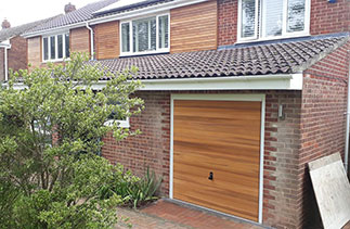 A Woodrite timber up and over garage door in the Buckingham range. In the Hardwick style. Finished in a Base coat light oak stain. With a white steel frame. Fitted in Winchester. Hampshire.