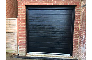 A Carteck 40mm insulated sectional garage door in  Center Rib style. In Black wood grain finish. With Black Ash pvc. Fitted in Camberley. Surrey.