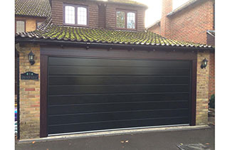 A Carteck 40mm insulated sectional garage door. In the Centre rib style. In a Black smooth finish. With Rosewood pvc around the frame. Fitted in Mytchet. Surrey.