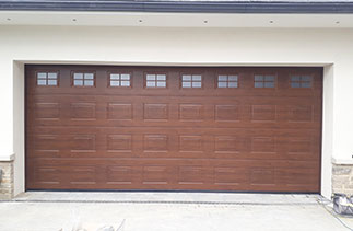 A Hormann deco grain sectional garage door in Dark Oak with matching frame side cover profiles. Complete with glazing. Fitted in Dorking, Surrey