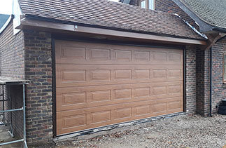 A Carteck Georgian sectional garage door in Winchester Oak with a Brown steel frame fitted between the opening. Fitted in Chobham, Surrey.